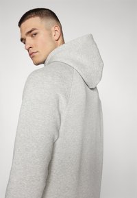Hoodie gris en tissu doux, doté d'une capuche avec cordon de serrage, de poignets côtelés et d'une coupe décontractée, avec une légère texture visible.