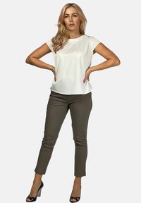 Biały, krótko rękawowy top zestawiony z dopasowanymi oliwkowymi spodniami. Stylizację dopełniają czarne sandały na obcasie z odkrytymi palcami. Gładkie tekstury w całej stylizacji.
