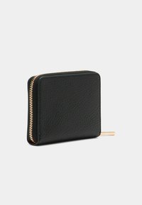 Portefeuille en cuir noir texturé avec fermeture éclair dorée, de forme rectangulaire, se tenant debout sur un fond gris clair uni.