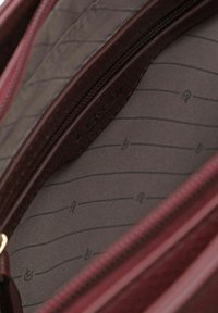 Innenseite einer kastanienbraunen Lederhandtasche mit zwei Reißverschlussfächern; ausgekleidet mit grauem Stoff, der dünne, dunkle Streifen und kleine Logos aufweist.