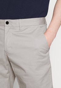 Shorts chino beige con una texture liscia, dotati di una tasca frontale, passanti per cintura e chiusura con un solo bottone in vita.
