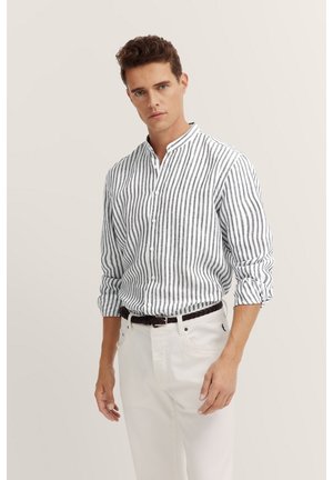 Gestreiftes Button-down-Hemd in Weiß und Marineblau, leichtes Material, Stehkragen, hochgekrempelte Ärmel, kombiniert mit weißen Hosen und einem geflochtenen Gürtel.