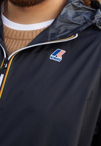 Giacca leggera nera con zip, con logo K-Way. Il colletto è regolabile e ci sono dettagli colorati sulla zip.