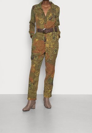 Camo-Jumpsuit in Erdtönen mit Blumen- und Leopardenmustern; verfügt über einen Kragen, lange Ärmel, Taschen und einen braunen Gürtel. Ergänzt durch Stiefeletten.