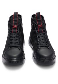 Paire de baskets montantes noires avec lacets noirs, languettes rouges cousues et logo "Hugo" sur la languette et la zone des orteils.