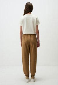 Crème t-shirt met korte mouwen, gecombineerd met bruin, taps toelopende joggingsbroek met elastische boorden en witte sneakers. Eenvoudige en comfortabele pasvorm.