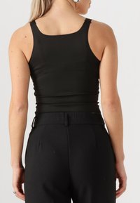 Top negro sin mangas con un diseño ajustado, textura suave y escote redondeado, combinado con pantalones negros de cintura alta.