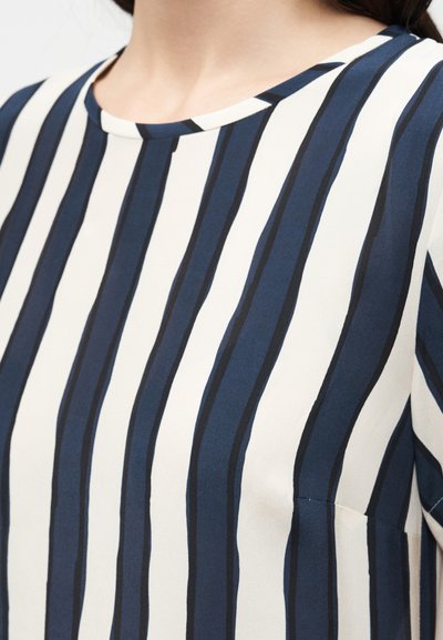 Κοντινό πλάνο ατόμου που φοράει πουκάμισο με κάθετες μπλε σκούρες και λευκές ρίγες και στρογγυλή λαιμόκοψη.