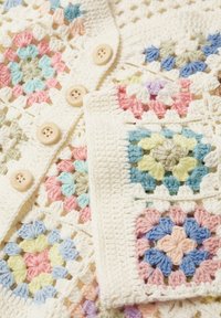 Cardigan au crochet avec une base crème et des carrés granny floraux colorés dans des teintes pastel. Comprend cinq boutons de couleur claire.