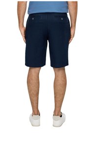 Shorts en lin bleu marine avec deux poches arrière dotées de boutons en métal, légèrement au-dessus du genou, associés à des baskets blanches.