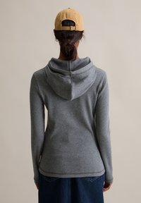 Grijze hoodie met een afgeronde capuchon en geribbelde structuur, gecombineerd met een denimrok. De capuchon heeft een naad langs de achterkant.