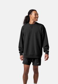 Felpa nera in pile con collo tondo, polsini e orlo a coste. Abbinata a pantaloni sportivi neri con un logo discreto.