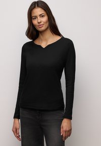 Czarna prążkowana bluzka z długim rękawem i dekoltem w kształcie litery V. Charakteryzuje się miękką teksturą i dopasowanym krojem, zestawiona z ciemnoszarymi dżinsami.