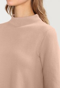 Stickad tröja i mjukt beige, med hög hals och långa ärmar. Tyget har en fin struktur och en avslappnad passform.