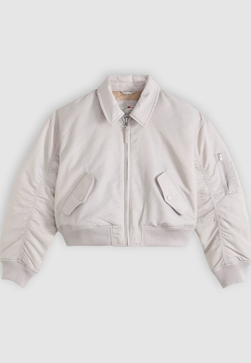 Veste bomber courte beige clair avec fermeture éclair frontale, poches à rabat boutonnées, poche zippée sur la manche, et poignets et ourlet côtelés.