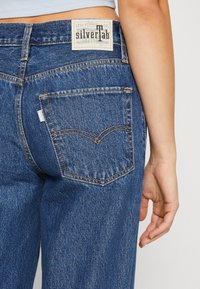 Modré džíny z denimu s vysokým pasem, s označením silverTab, oranžovým prošitím a zadní kapsou s výrazným zakřiveným švem.