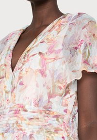 Blumenmuster-Kleid aus leichtem, durchscheinendem Stoff. Mit tiefem V-Ausschnitt, Rüschensäulen und gerafftem Taillenbereich mit zarten Faltendetails.