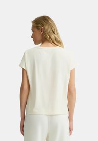 Top crema a maniche corte con vestibilità rilassata, scollo rotondo e texture liscia. Presenta delle aperture laterali all'orlo per facilitare i movimenti.