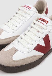 Sneakers bianchi con accenti rossi, dotati di punta in suede e pannello laterale, lacci spessi e dettagli cuciti. Suola in gomma con battistrada.