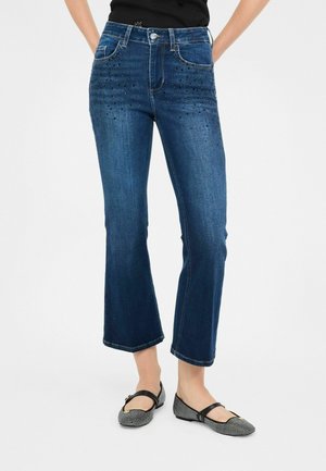 Jeans cropped in denim blu scuro con decorazioni in perline sulla parte anteriore, cinque tasche, passanti per cintura e chiusura a bottone classica.