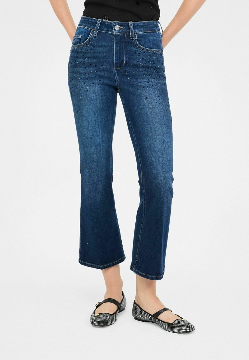 Jeans recortados de mezclilla azul oscuro con adornos de cuentas en la parte delantera, cinco bolsillos, trabillas para cinturón y un cierre clásico con botón.