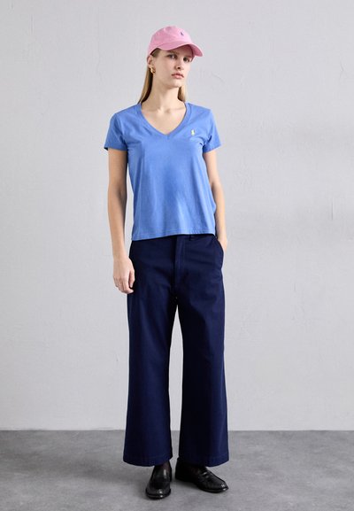 Blue cotton v-neck t-shirt, navy wide-leg trousers, pink baseball cap, and black shoes. Minimal design with subtle logo embroidery on the shirt.