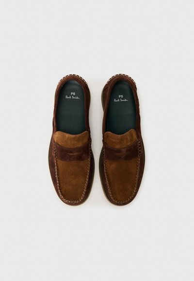 Mocassins en suede marron avec une bande contrastante de brun clair, des accents cousus et une semelle en caoutchouc plate. L'intérieur présente un logo.
