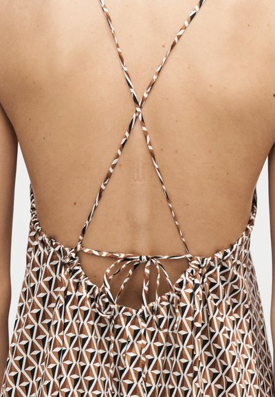 Πλάτη ενός ατόμου που φοράει φόρεμα με γεωμετρικό σχέδιο σε καφέ, άσπρο και μαύρο χρώμα, με λεπτές σταυρωτές τιράντες δεμένες στο κάτω μέρος της πλάτης.