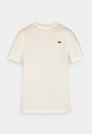 T-shirt en coton couleur crème avec un col rond classique, des manches courtes et un logo de crocodile vert brodé sur la poitrine gauche.