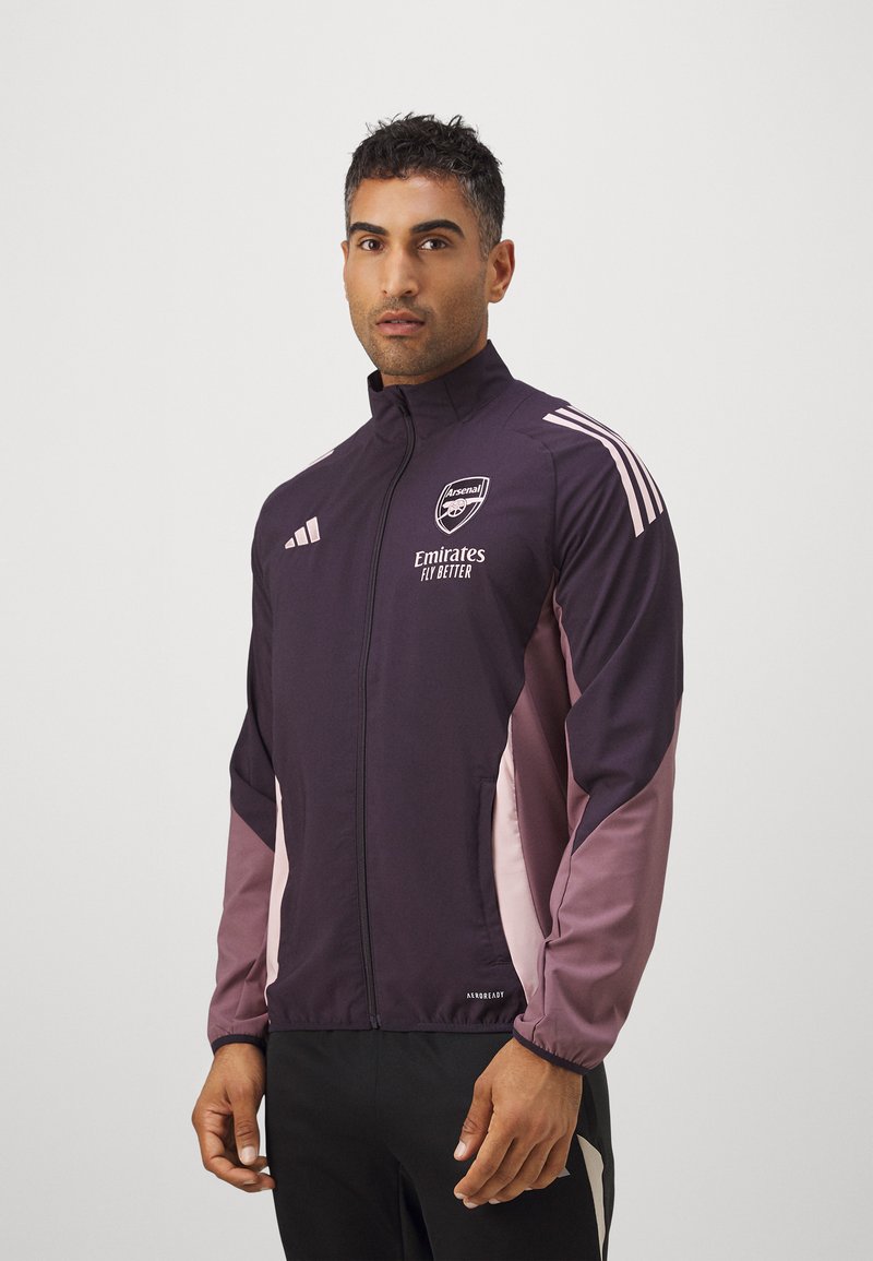 Dark purple and pink athletic jacket with a high collar, zip front, and white Adidas stripes; features Arsenal logo and 'Emirates' text.