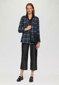 Karierter Blazer in Marineblau und Blau, schwarzes Hemd, schwarze, cropped Lederhosen, schwarze Loafers. Kleine schwarze Umhängetasche mit Logodetail.