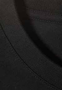 Black cotton T-shirt collar showing ribbed texture, with visible stitching details and smooth fabric. Close-up of neckline and fabric.