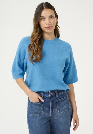 Helles blaues, kurzärmliges Sweatshirt aus weichem Strickstoff mit rundem Halsausschnitt und dezenten Raglan-Schulternähten, kombiniert mit hoch taillierten Jeans.
