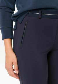Marine sportieve broek met een ritszak aan de zijkant, zachte textuur, aansluitend ontwerp en contrasterende taillebanddetail.