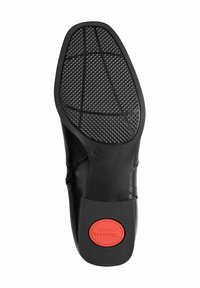 Fekete bőr cipőtalp texturált gumitalppal, kör alakú piros hangsúlyos résszel, amelyen a "Toms Comfort" felirat található. Strukturált, modern kialakítás.