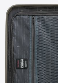 Vnitřek tvrdého kufru v šedé tkanině s jemnou síťovanou kapsou, několika zipovými přihrádkami a štítkem s informacemi o produktu.