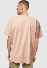 Lichtroze oversized t-shirt, korte mouwen, zachte katoenen stof, ronde hals, eenvoudig ontwerp, losse pasvorm, van achteren gezien.