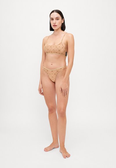 Nude lace bikini set featuring a bralette with thin straps and a matching thong. Both have a subtle circular pattern and elastic trim.