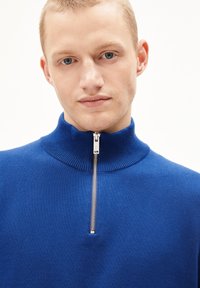 Pull-over en tricot bleu avec col montant et fermeture éclair sur le devant ; présente un col côtelé et une texture lisse.