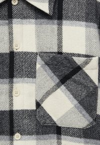 Zwarte, grijze en witte geruite overhemdsectie met een knoopsluiting aan de voorkant en een gepatternde borstzak met diagonale en vierkante ontwerpen.