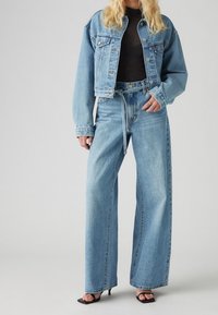 Ljusblå denimjacka med en kort passform, i kombination med vida ljusblåjeans och svarta klacksandaler. Har en avslappnad design.