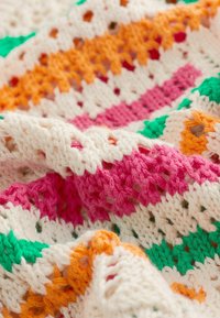 Bunt gehäkelte Decke mit Streifen in Rosa, Orange, Grün und Creme, die ein strukturiertes, offenes Webmuster aufweist.