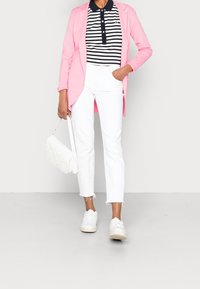 Różowa marynarka, polo w granatowo-białe paski, białe spodnie, biała torba o plecionym wzorze i białe sneakersy. Casualowy i nowoczesny układ stroju.