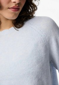 Ljusblå stickad tröja med rundad halsringning och mjuk textur, med raglanskärning och en något avslappnad passform.