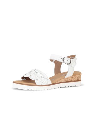 White sandal with braided front strap, ankle strap with silver buckle, cork wedge heel, and white ridged sole.