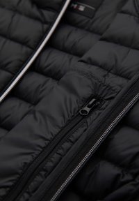 Gros plan d'une veste matelassée noire avec deux fermetures éclair noires montrant le rembourrage et les détails de couture.