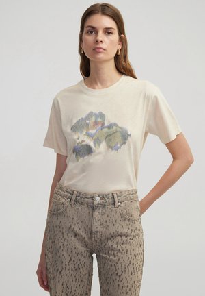 T-shirt beige clair à manches courtes avec un design graphique abstrait coloré. Assorti à un jean beige texturé avec des motifs sombres.