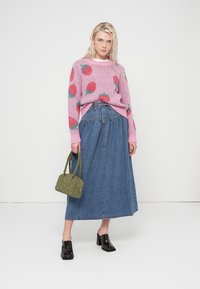 Ροζ πλεκτό πουλόβερ με κόκκινα μοτίβα φράουλας, συνδυασμένο με μακριά τζιν φούστα και τσάντα ώμου χακί. Μαύρα παπούτσια με χοντρό τακούνι.