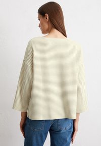 Haut rayé jaune clair avec une coupe ample et des manches larges, en tissu texturé. Associé à un jean bleu, vu de dos.