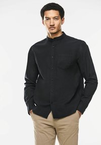 Schwarzes Hemd mit Knopfleiste, Stehkragen und langen Ärmeln. Verfügt über eine einzelne Brusttasche und einen glatten, strukturierten Stoff.